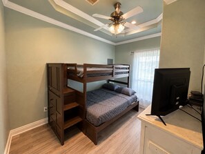 A bedroom with a bunk bed, a desk with a television, and a ceiling fan. - Our house is not fancy; it is welcoming. (Bolivar Peninsula)