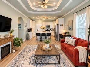 A modern living room with a fireplace, a red sofa, a coffee table, and a TV. - Our house is not fancy; it is welcoming. (Bolivar Peninsula)