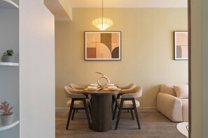 A dining area with a round table, four chairs, a pendant light, and a framed abstract painting on the wall. - 2BR Corner | King + Queen | Soho D1 | Floor 24 (Thành phố Hồ Chí Minh)