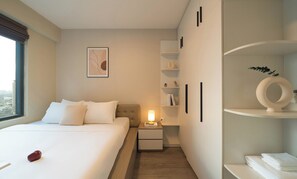 A hotel room with a bed, bedside table, lamp, and a view of the city. - 2BR Corner | King + Queen | Soho D1 | Floor 24 (Thành phố Hồ Chí Minh)