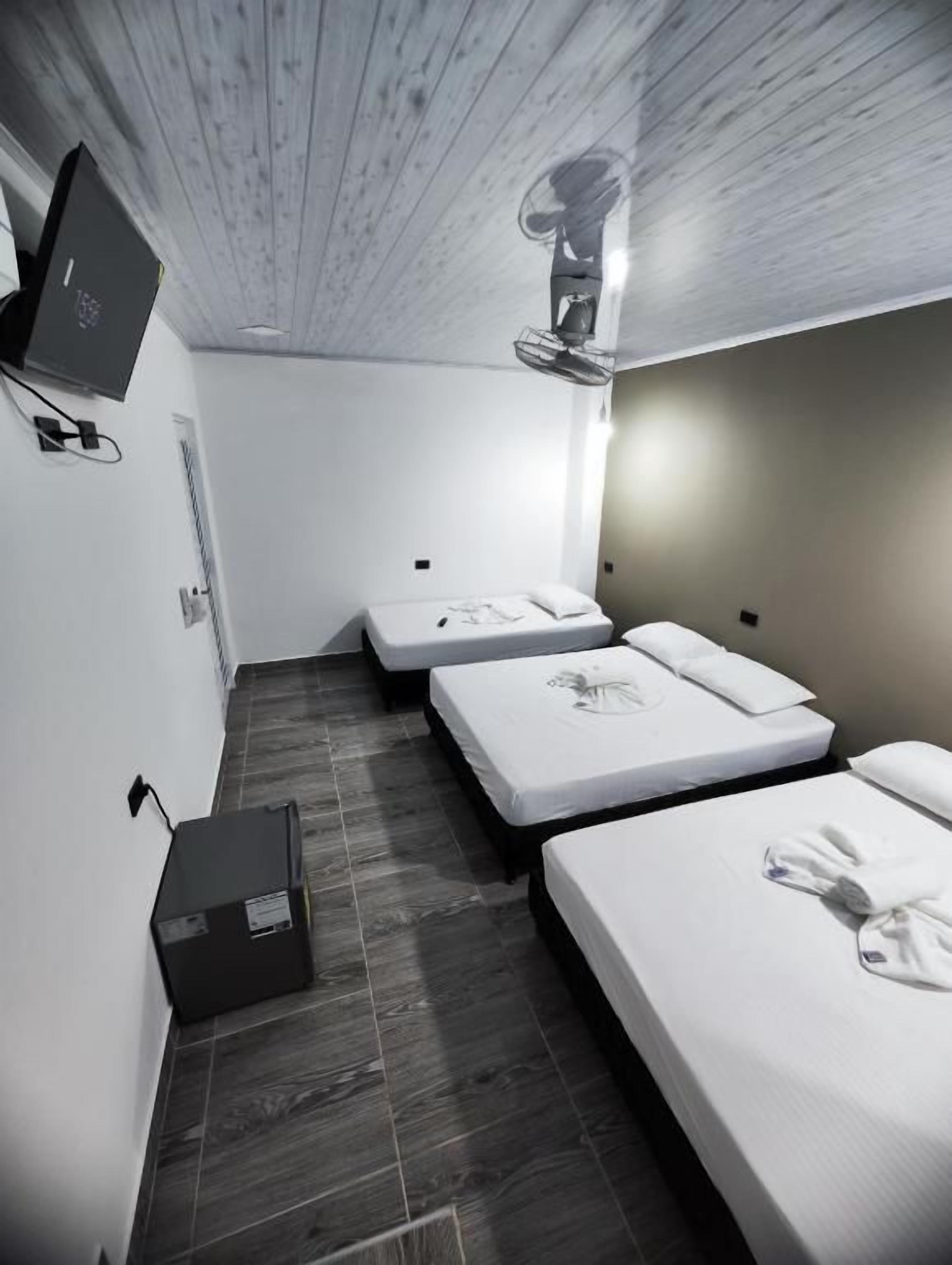 Ein Hotelzimmer mit zwei Betten, einem Flachbildfernseher, einem Deckenventilator und einem kleinen Schreibtisch mit einem Computer.