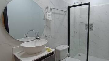 Un baño con un espejo redondo, un lavabo, un inodoro y una ducha con mampara de cristal.
