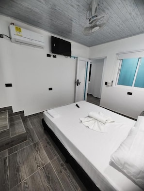 Habitació d'hotel amb un llit, televisió, finestra i porta.