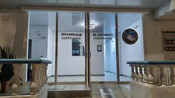 Fachada de un hotel con puertas de vidrio, una escalera y un mostrador de recepción.