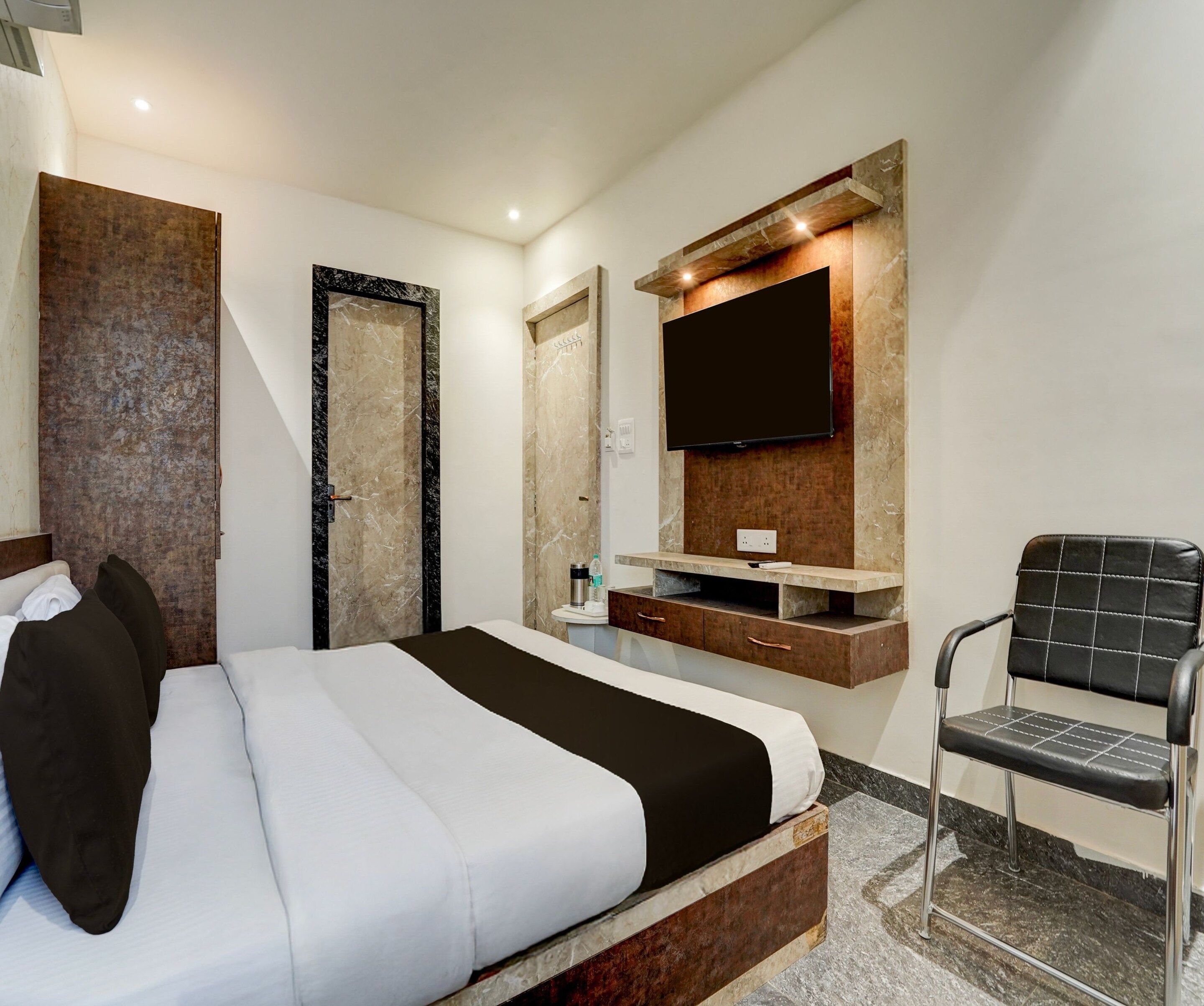 A modern hotel room with a bed, a TV mounted on the wall, a chair, and a bathroom with a shower.