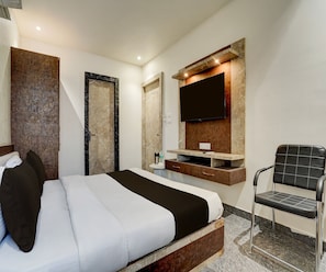 Ein modernes Hotelzimmer mit Bett, Wandfernseher, Sessel und Badezimmer mit Dusche.