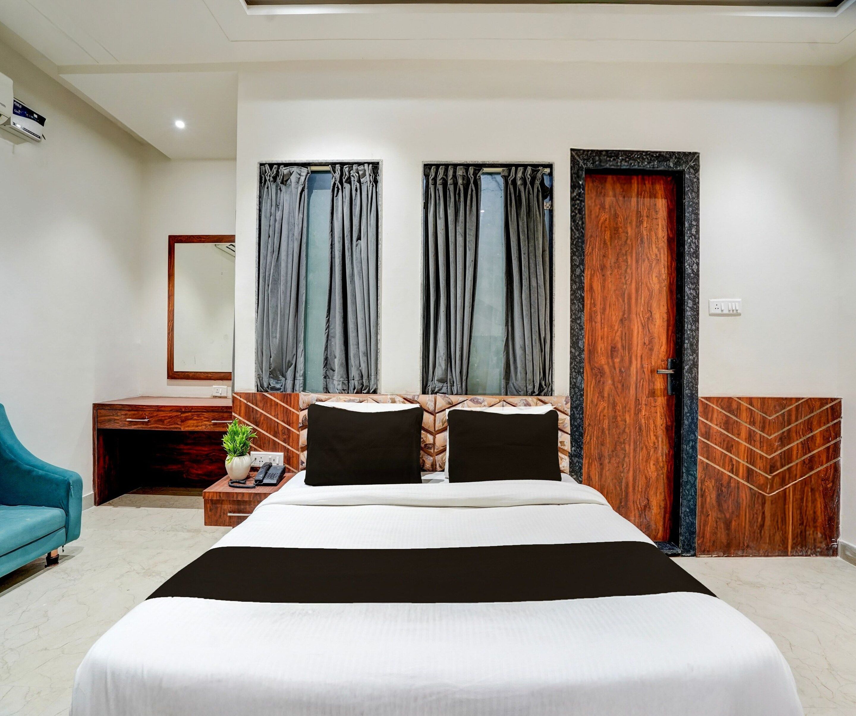 A modern hotel room with a large bed, a desk with a telephone, a blue chair, and a wardrobe.