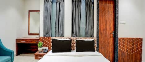 A modern hotel room with a large bed, a desk with a telephone, a blue chair, and a wardrobe.