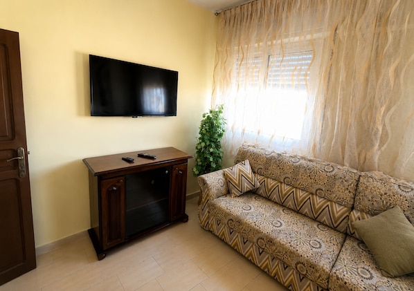Un soggiorno con TV a schermo piatto montata a parete, mobile TV in legno, divano decorato e una finestra con tende leggere.