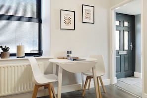 A dining area with a table and chairs, a radiator, a window with blinds, and a door. - Serene 2BR Stay in Penrith | Sleeps 4+Parking+WiFi (Penrith)