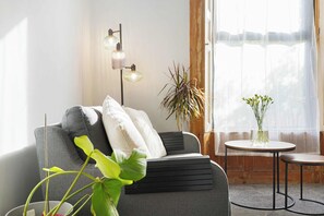 A modern living room with a sofa, a floor lamp, a potted plant, and a small table with a vase. - Serene 2BR Stay in Penrith | Sleeps 4+Parking+WiFi (Penrith)
