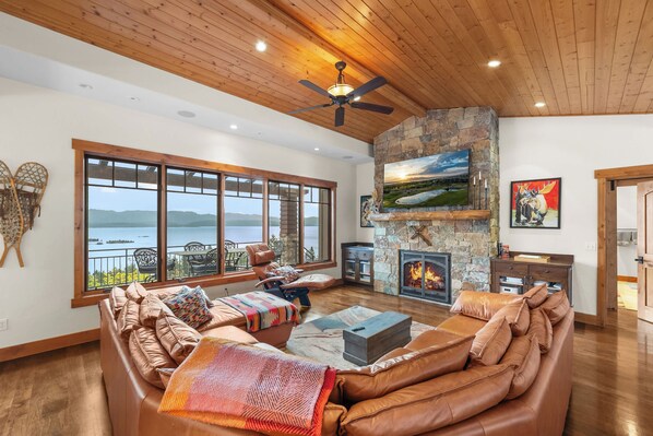 A spacious living room with a stone fireplace, leather sofas, and a large window overlooking a lake. - Lakeview Retreat - 4BR Home (Somers)