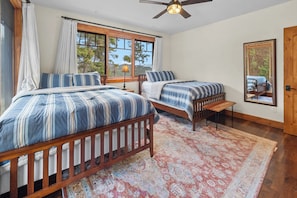 A bedroom with two beds, a ceiling fan, and a large window with curtains.