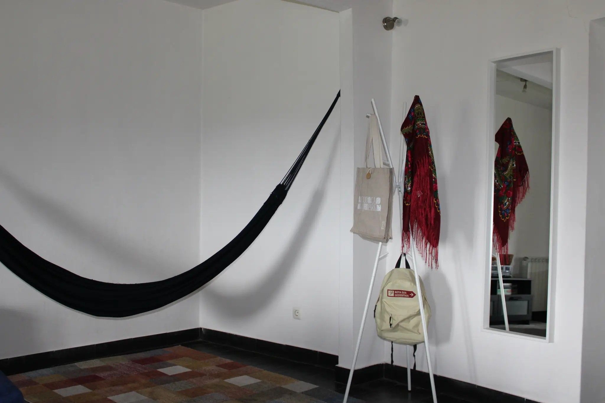 Una habitación con una hamaca, un bolso colgante y un espejo que refleja un papel tapiz estampado.