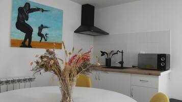 Een moderne keuken met een witte tafel, een vaas gedroogde bloemen, een schilderij aan de muur en een zwarte afzuigkap.