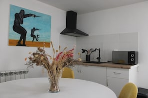 A modern kitchen with a white table, a vase of dried flowers, a painting on the wall, and a black range hood.