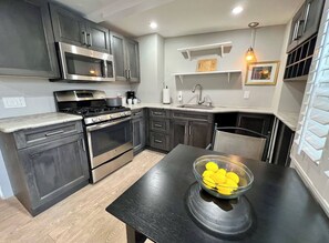 Cocina moderna con armarios oscuros, electrodomésticos de acero inoxidable y un comedor con mesa negra y un tazón de limones.