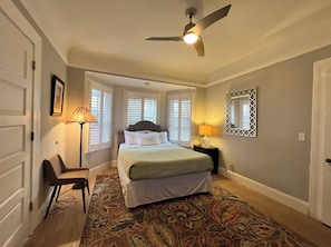 Una camera da letto con un letto, una sedia, una lampada da terra, un ventilatore a soffitto e un tappeto decorato.