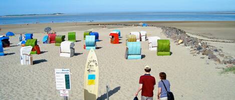 Una playa arenosa con coloridas cabañas de playa y un letrero de tablas de surf.