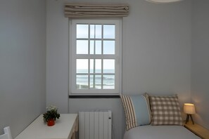 Un dormitorio con ventana vista al mar, una mesita de noche con lámpara y un radiador.