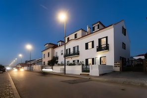 A modern two-story building with a balcony on the second floor, a gated entrance, and a street with cars and streetlights.