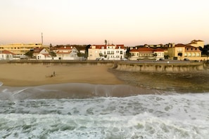A beach with a sandy shore and waves, buildings in the background, and a clear sky.