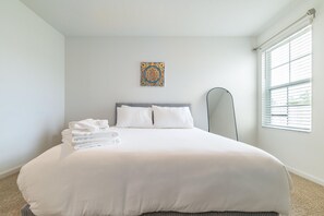 A hotel room with a large bed, a bedside mirror, and a window with blinds. - Modern 3BR Townhome | 30-Day Minimum (Jacksonville)