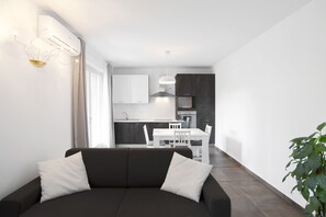 A modern living room with a dark sofa, white cushions, and a dining area with a white table and chairs. - Apartment 'Dama' with Private Terrace, Wi-Fi and Air Conditioning (Bardolino)