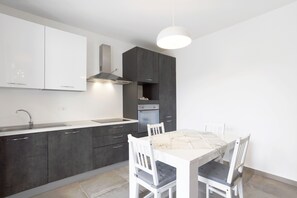 Eine moderne Küche mit Esstisch und Stühlen, einem eingebauten Backofen und einer Pendelleuchte.