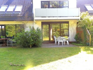 A two-story house with a patio area featuring a table and chairs, surrounded by greenery. - 12 / Waldstrasse (Wyk auf Foehr)