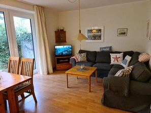 A living room with a sofa, a coffee table, a TV, and a dining table with chairs. - 12 / Waldstrasse (Wyk auf Foehr)