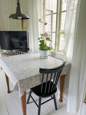 A dining area with a table set for two, a potted plant, and a television on a stand. - Cottage by Lake Ralången with alpacas and horses (Aneby)
