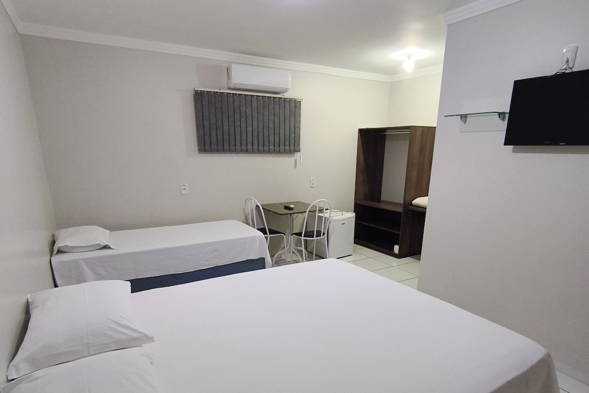 Een hotelkamer met een bed, bureau, stoel, televisie en airconditioning.