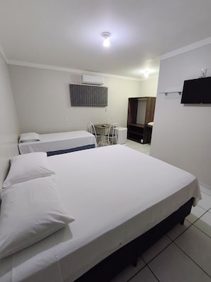 Een hotelkamer met een bed, bureau, stoel, televisie en airconditioning.