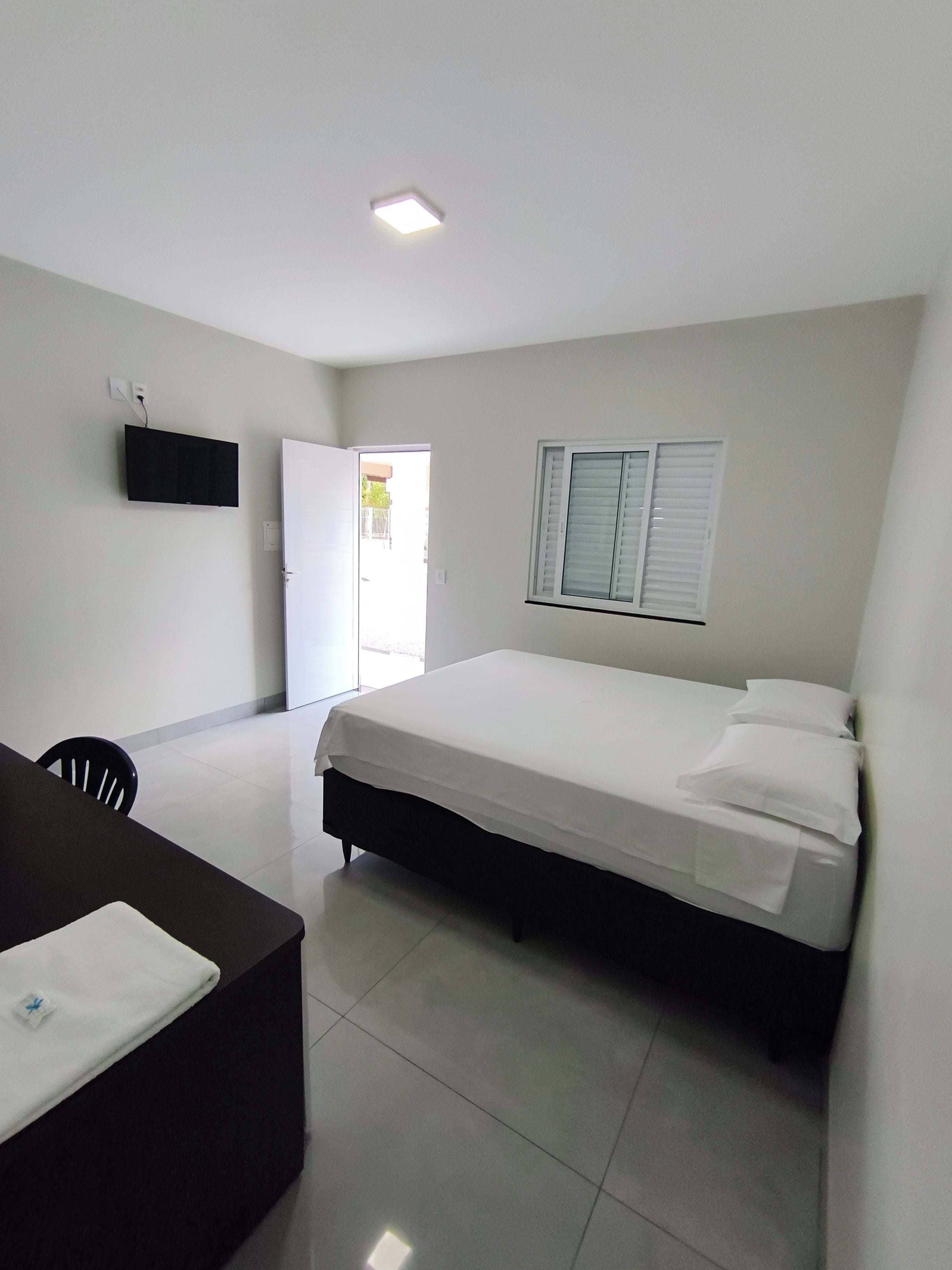 Une chambre d’hôtel comprenant un lit, un bureau, une chaise, un téléviseur fixé au mur et une fenêtre avec des stores.