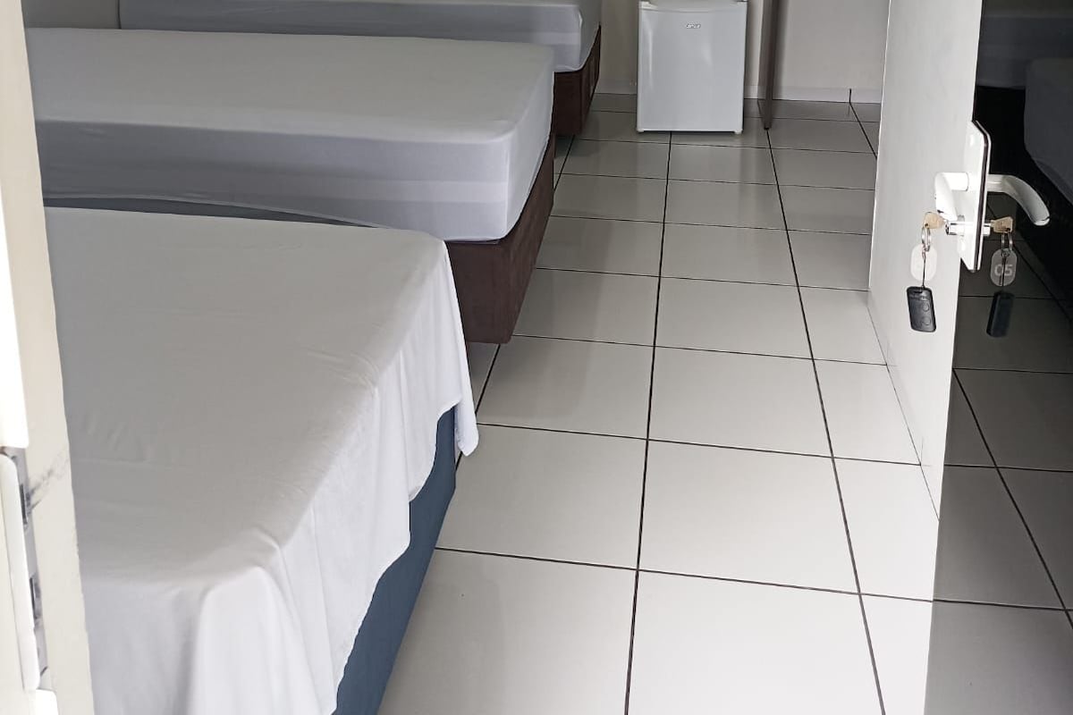 Een hotelkamer met twee eenpersoonsbedden, een tafeltje, een wandairconditioner en een betegelde vloer.