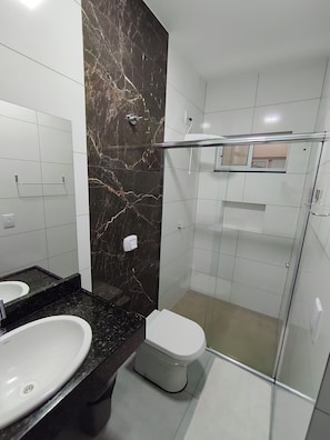 A modern bathroom with a marble wall, a glass shower enclosure, a white sink, and a toilet. - Hotel Flor de Ipê (Sorriso)