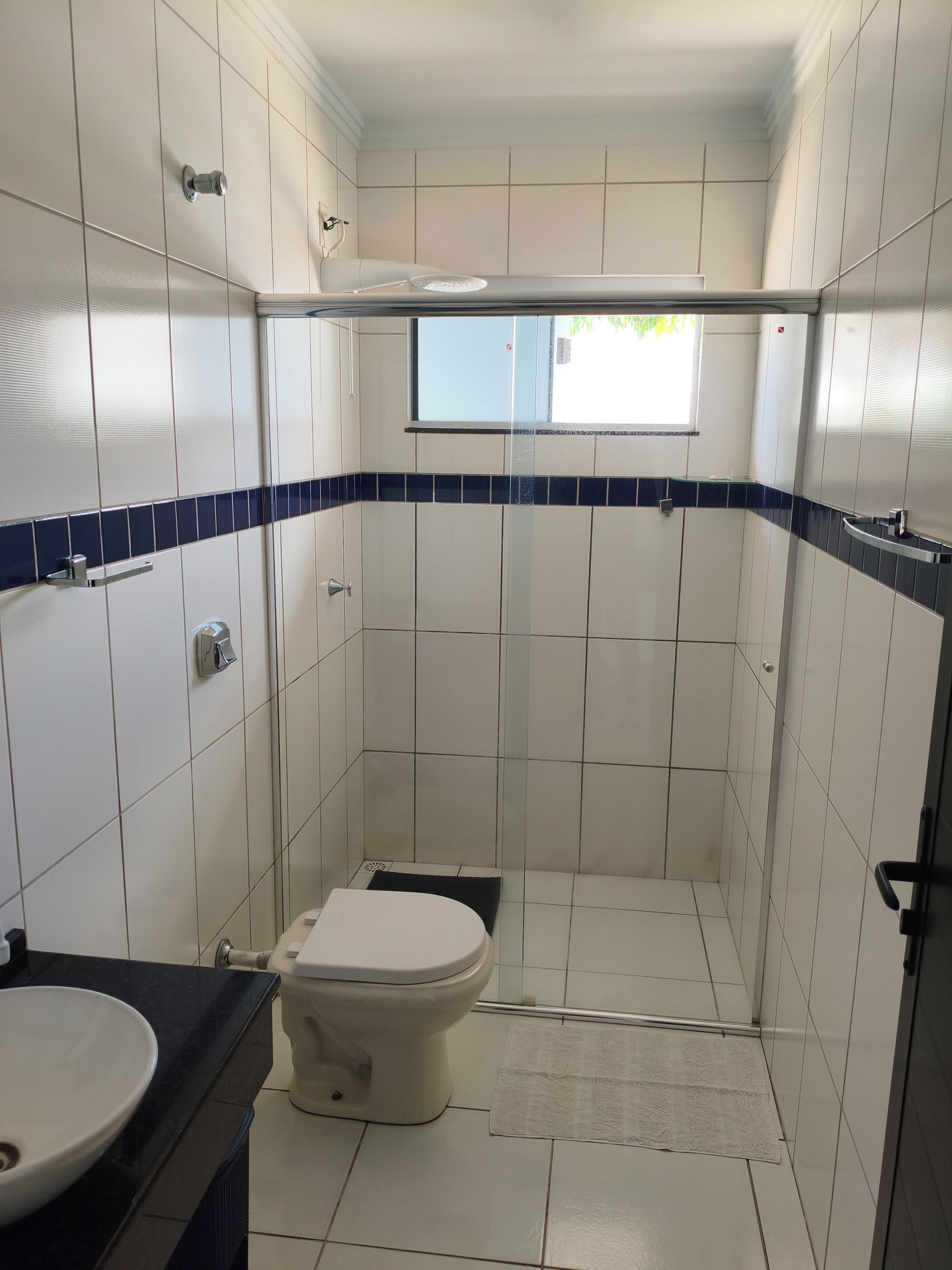 Une petite salle de bain avec des carreaux blancs, des toilettes, un lavabo et un espace douche.