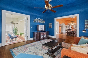 A spacious living room with a blue accent wall, a ceiling fan, a flat-screen TV, and a dining area with a chandelier. - La Amante Del Verano a Luxury Spanish-Style Retreat with Pool that Sleeps 15 (Lakeland)