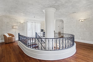 A spacious living area with a wooden floor, a white column, and a black wrought iron railing. - La Amante Del Verano a Luxury Spanish-Style Retreat with Pool that Sleeps 15 (Lakeland)