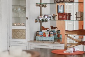 A kitchen with a glass cabinet containing glassware, a shelf with a model train, and a wicker basket with jars. - La Amante Del Verano a Luxury Spanish-Style Retreat with Pool that Sleeps 15 (Lakeland)