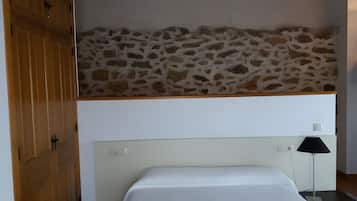 Een slaapkamer met een stenen muur, een bed, een nachtkastje en een houten garderobe.