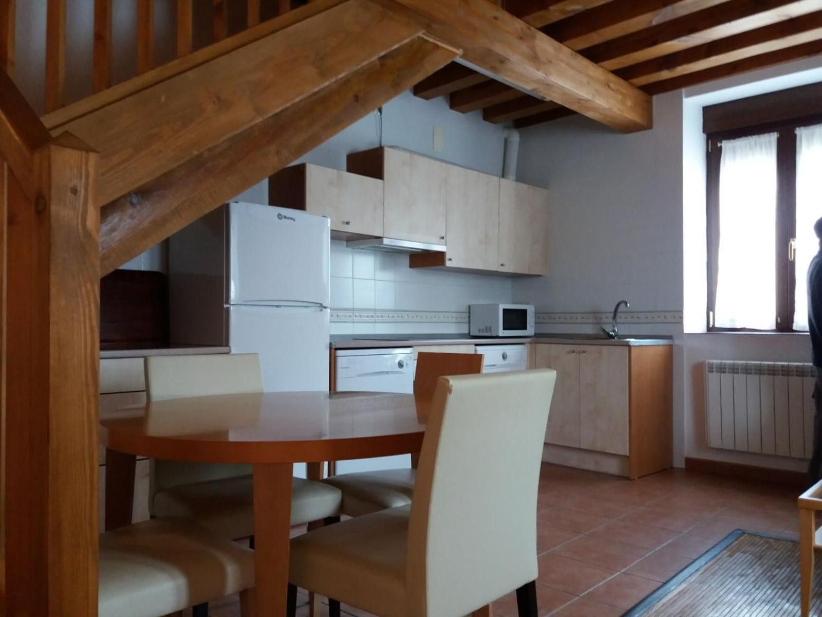 A kitchen with wooden beams, white cabinets, a white refrigerator, a microwave, and a dining table with chairs.