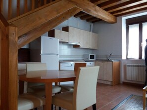A kitchen with wooden beams, white cabinets, a white refrigerator, a microwave, and a dining table with chairs. - Country House 'Casa Rural La Antigua Fragua' (Los Llanos de Tormes)