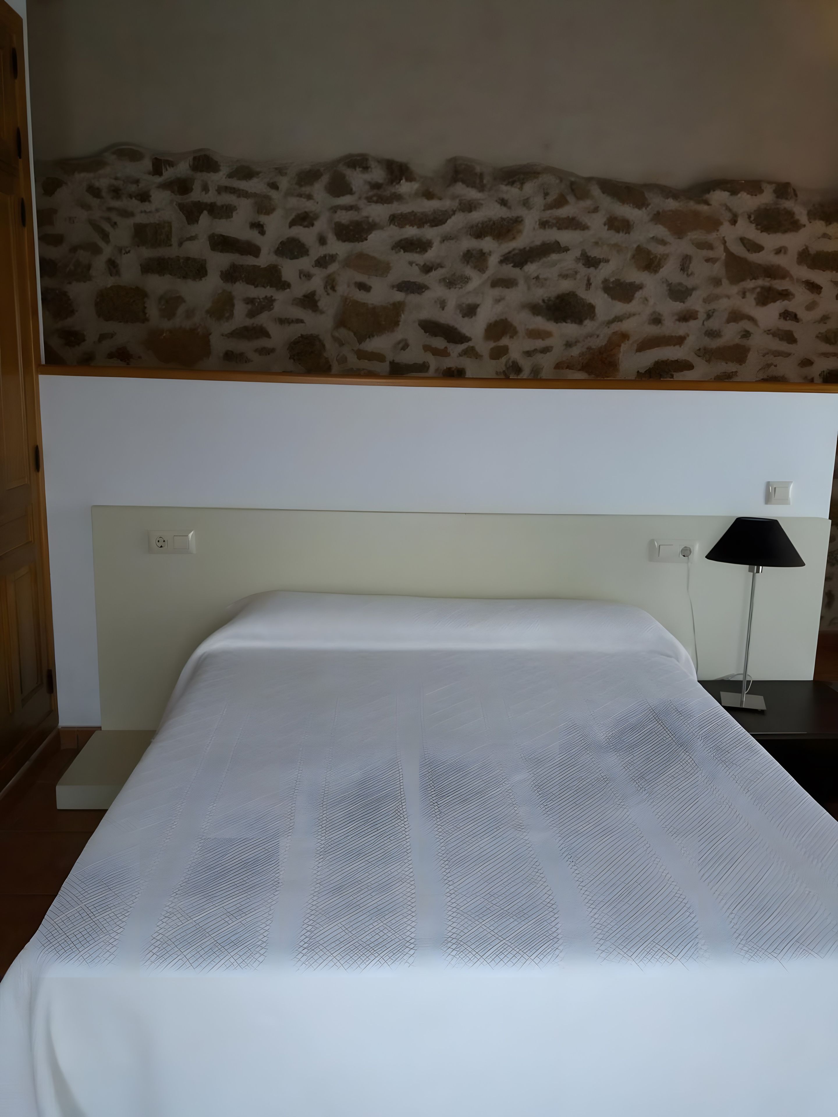 Ein Bett mit weißer Matratze und einem Kopfteil an einer Steinwand.