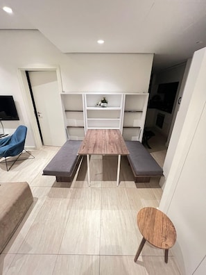 Una sala de estar moderna con una mesa de madera, dos bancos, una mesita redonda y estanterías empotradas.