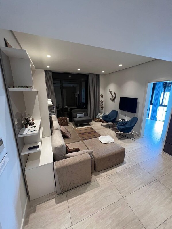 Una sala de estar moderna con un sofá modular, un televisor de pantalla plana y un comedor con mesa y sillas.