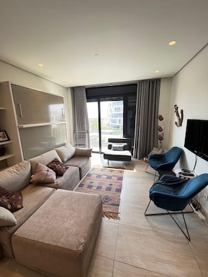 Una sala de estar moderna con un sofá, una mesa de centro, un televisor y un balcón con vistas.
