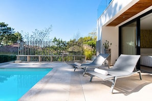 A modern outdoor pool area with two lounge chairs and a glass-enclosed bedroom. - Villa Balis - Seignosse - Pool - Golf - Beach (Seignosse)