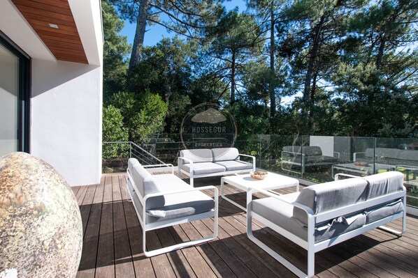 Ein moderner Außenbereich zum Sitzen mit einer Holzterrasse, weißen Möbeln und einem Schild mit der Aufschrift 'HOSSEGOR PROPERTIES'.